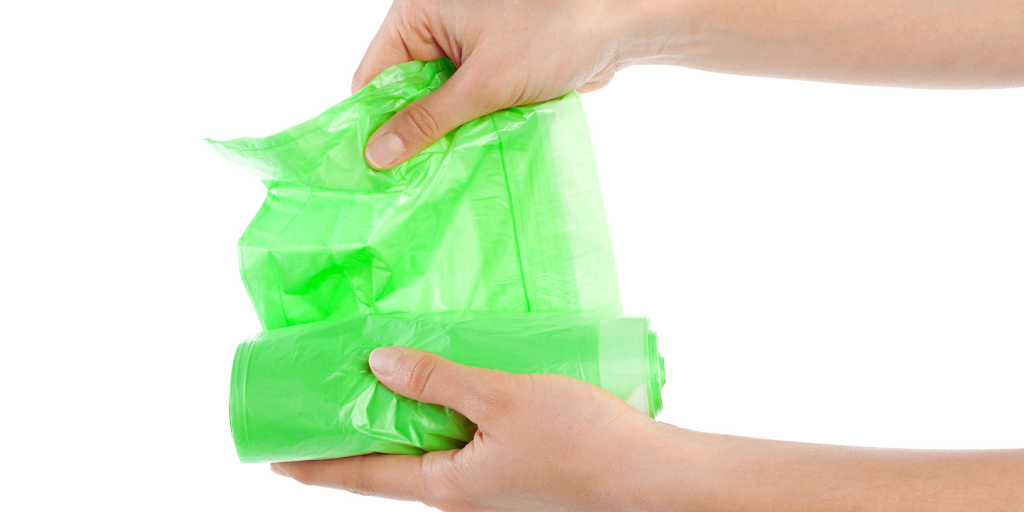 a person holding a roll of green garbage bags