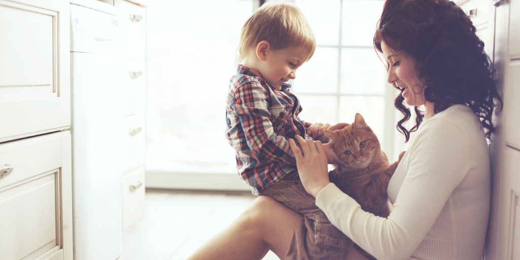a women holding a child and cat on her lap sitting on the floor.